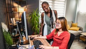 Two young businesswomen collaborating on a computer project in a modern office